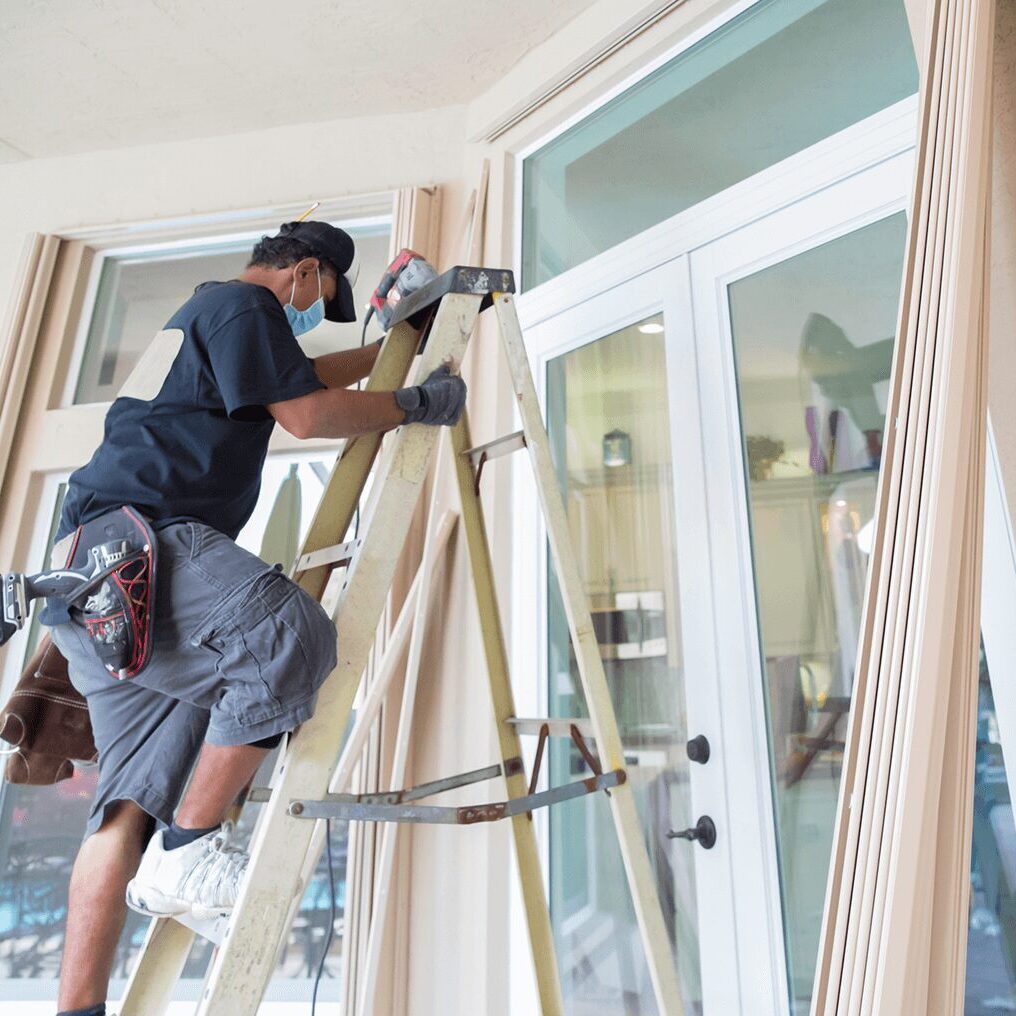 Worker installing window shutters on ladder.